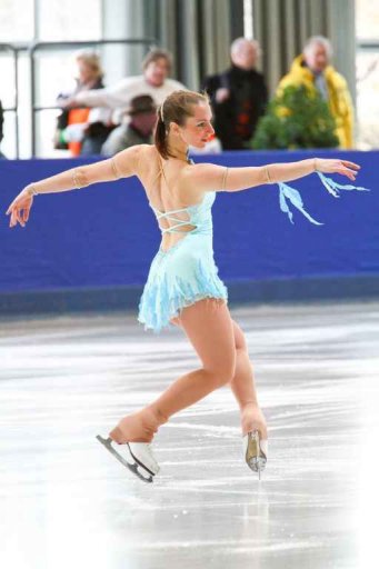CP on the ice, arms stretched out, balancing on the toes, audience blurred in the background